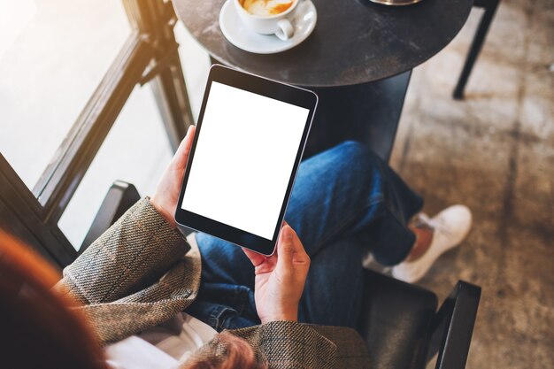 Immagine mockup vista dall'alto di una donna seduta e in possesso di un tablet pc nero con schermo desktop bianco vuoto