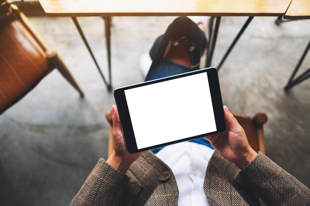 Immagine mockup vista dall'alto di una donna seduta e in possesso di un tablet pc nero con schermo desktop bianco vuoto