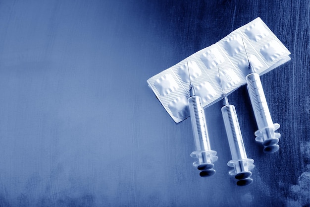 Immagine monocromatica blu di siringhe e confezione di pillole