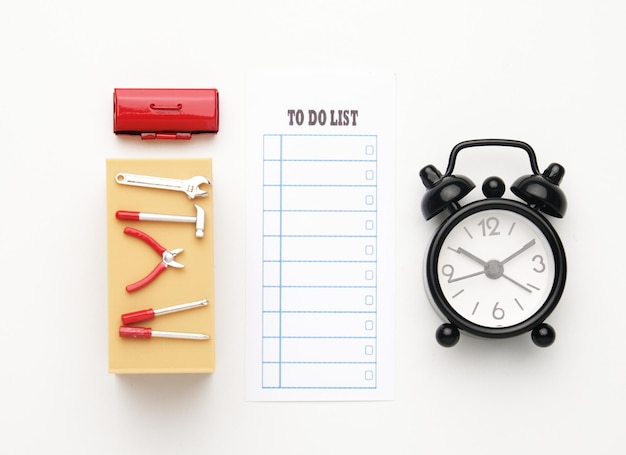 Immagine piatta di strumenti in miniatura sulla scrivania dell'ufficio, cassetta degli attrezzi in miniatura, sveglia e carta con l'elenco delle cose da fare