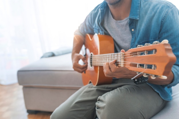 Immagine potata dell&#39;uomo bello in abbigliamento casual che gioca chitarra a casa