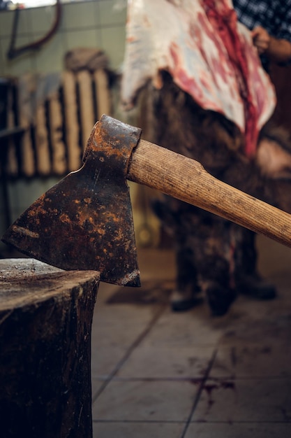 Immagine ravvicinata dell'ascia di carne sopra il macellaio barbuto taglia la carcassa del maiale selvatico sullo sfondo.