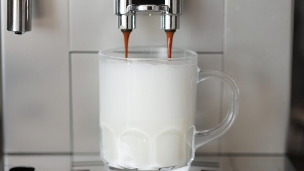 Immagine ravvicinata di caffè che si versa in una tazza di vetro con latte che fa cappuccino utilizzando la macchina da caffè automatica Bevanda per colazione