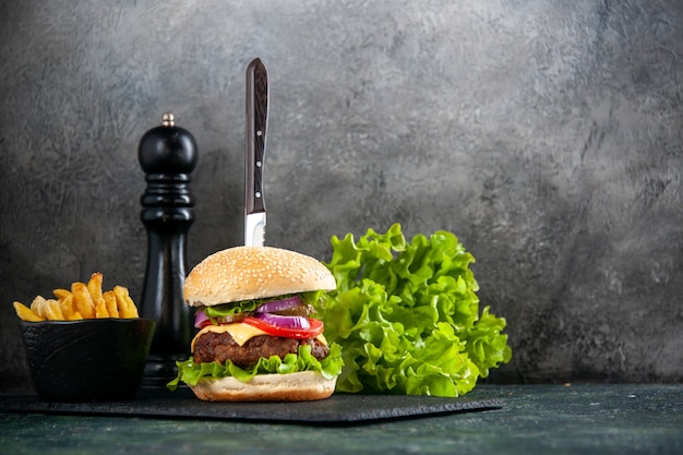 Immagine ravvicinata di coltello in un delizioso sandwich di carne e patatine verdi su vassoio nero su superficie grigia