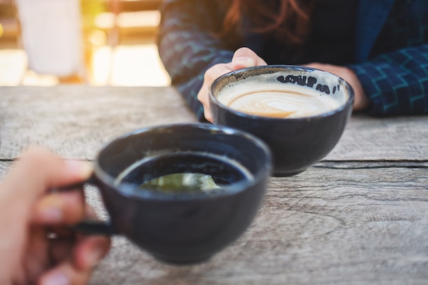 Immagine ravvicinata di due persone che fanno tintinnare tazze da caffè su un tavolo di legno