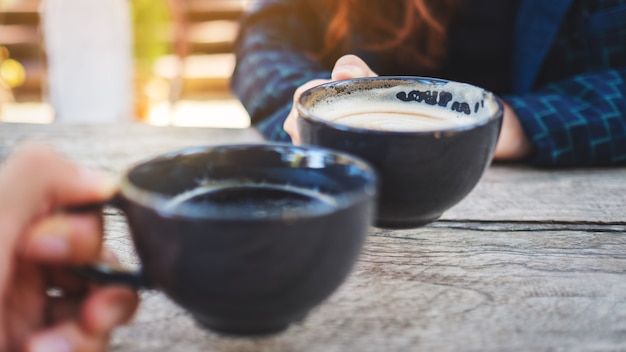 Immagine ravvicinata di due persone che fanno tintinnare tazze da caffè su un tavolo di legno