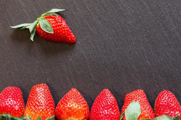 Immagine ravvicinata di fragole rosse fresche sdraiate su un tavolo di pietra nera