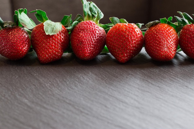 Immagine ravvicinata di fragole rosse fresche sdraiate su un tavolo di pietra nera