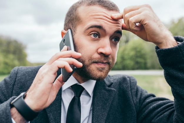 Immagine ravvicinata di un bel giovane uomo d'affari europeo urbano che utilizza gadget mobili all'aperto Imprenditore dall'aspetto alla moda che fa chiamate d'affari parlando su smartphone con un aspetto serio e preoccupato