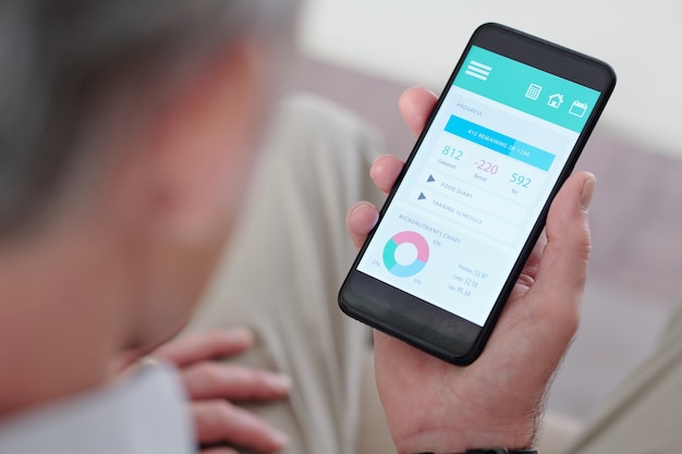 Immagine ravvicinata di un uomo anziano che controlla il grafico dei micronutrienti e le calorie consumate sullo smartphone