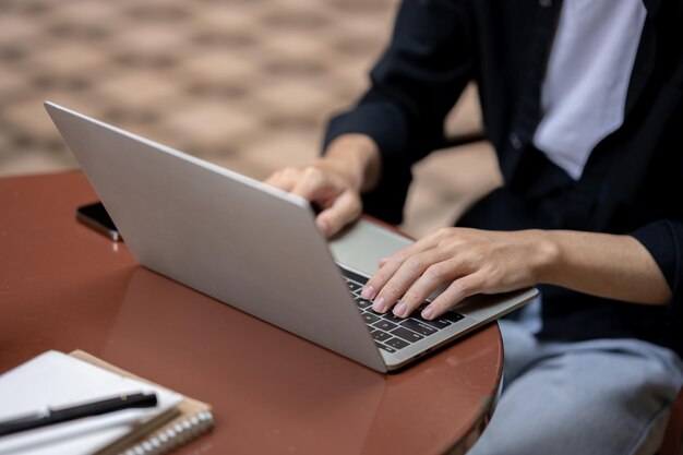 Immagine ravvicinata di un uomo che usa il suo computer portatile seduto a un tavolo all'aperto e lavora in remoto