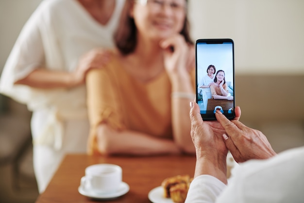 Immagine ravvicinata di una donna anziana che fotografa le sue amiche abbracciate sullo smartphone