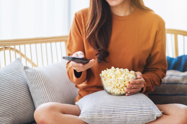 Immagine ravvicinata di una donna che mangia pop corn e cerca un canale con il telecomando per guardare la tv mentre è seduta sul divano di casa