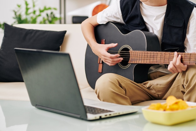 Immagine ritagliata dell'adolescente creativo che suona la chitarra e scrive una nuova canzone