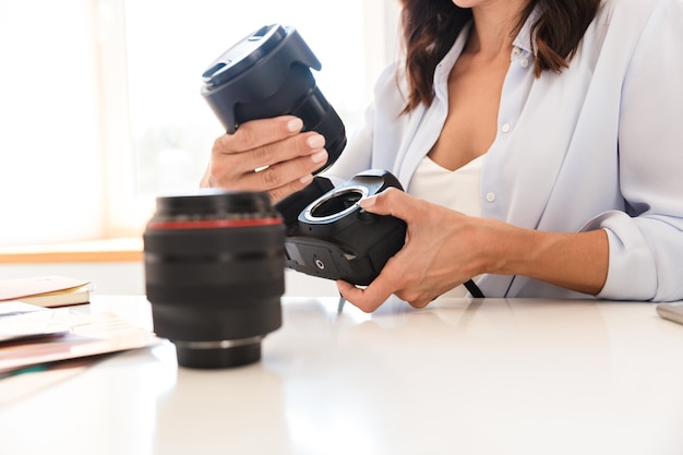 Immagine ritagliata della donna fotografa in ufficio seduta al tavolo con gli obiettivi della fotocamera.