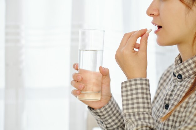 Immagine ritagliata della giovane donna che prende compressa anticoncezionale e bicchiere d'acqua