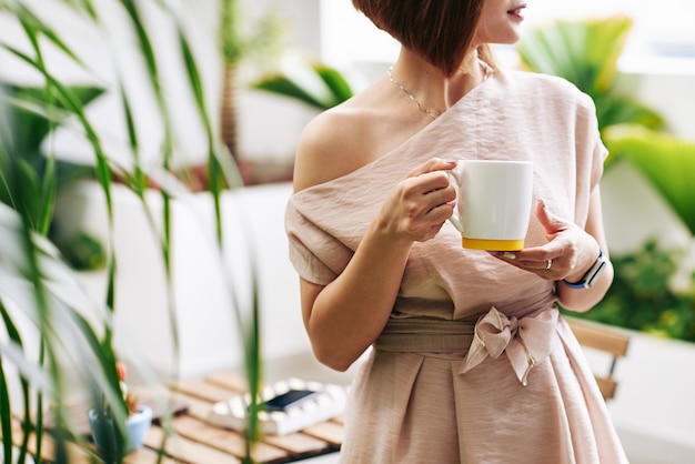 Immagine ritagliata della giovane donna in piedi con una grande tazza di caffè o tè caldo