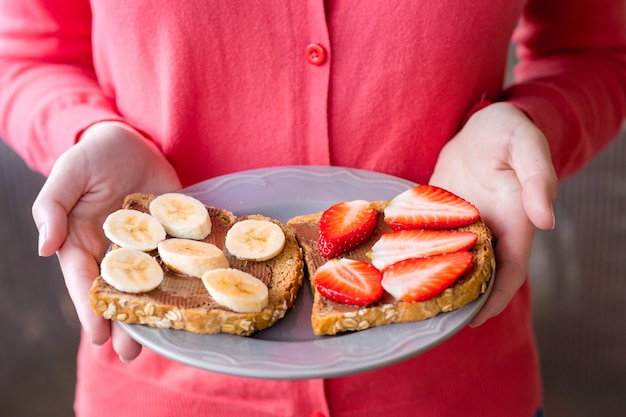 Immagine ritagliata della ragazza che tiene il piatto con toast di pasta di cioccolato e frutta