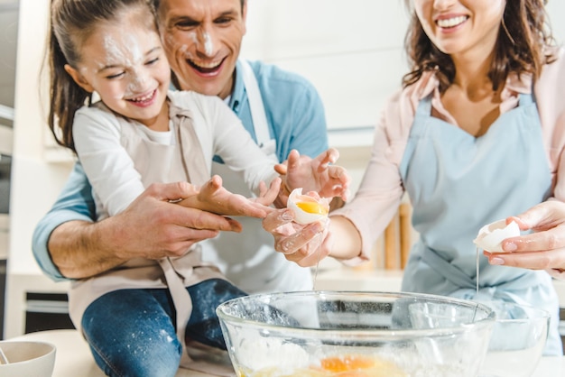 immagine ritagliata di famiglia felice che divide l'uovo nella ciotola in cucina