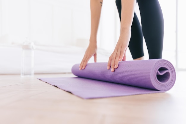 Immagine ritagliata di giovane donna che indossa abbigliamento sportivo tappetino da yoga con bottiglia d'acqua che si prepara per fare yoga Allenarsi a casa o nello studio di yoga Abitudini sane mantenersi in forma concetti di perdita di peso