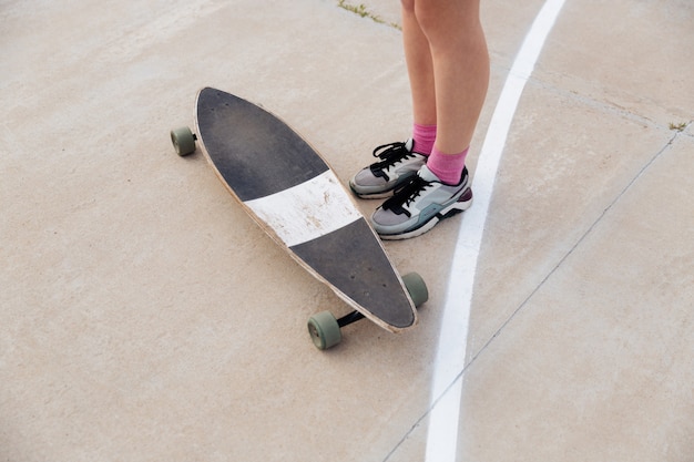 Immagine ritagliata di giovani gambe femminili e skateboard all'aperto sopra bianco