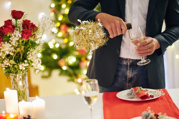 Immagine ritagliata di un giovane che versa un bicchiere di champagne alla festa di Natale