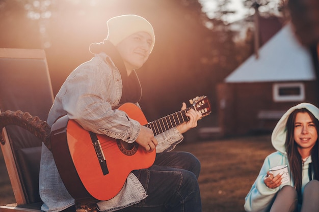 Immagine ritagliata di un ragazzo con una chitarra in mano che suona musica d'atmosfera. Nelle vicinanze, le amiche con la felpa blu sono sedute in un abbraccio e si godono la melodia.