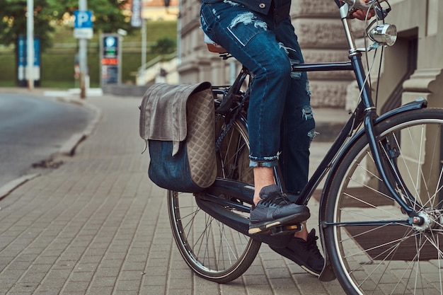 Immagine ritagliata di un uomo alla moda in abiti eleganti in sella a una bicicletta da città.