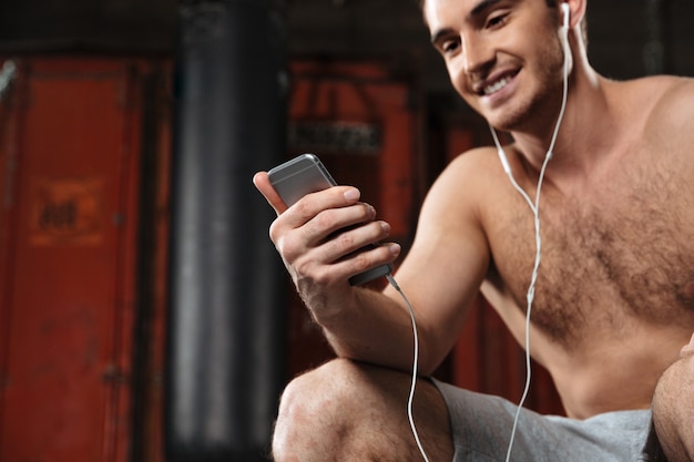 Immagine ritagliata di un uomo felice seduto in palestra mentre ascolta la musica per telefono.