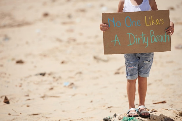 Immagine ritagliata di una bambina che tiene un cartello senza che a nessuno piace un'iscrizione sulla spiaggia sporca