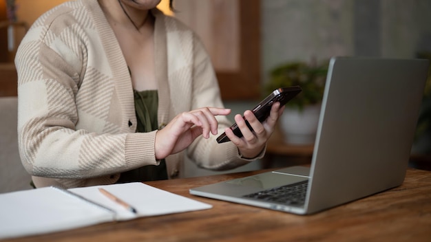 Immagine ritagliata di una donna asiatica che usa il suo smartphone mentre lavora in remoto in un bar