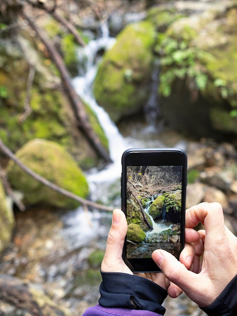 Immagine ritagliata di una donna che fotografa una cascata in una foresta Escursionismo e turismo naturalistico