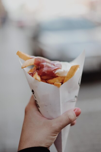 Immagine ritagliata di una donna con la mano che tiene delle patatine fritte con ketchup in un sacchetto di carta