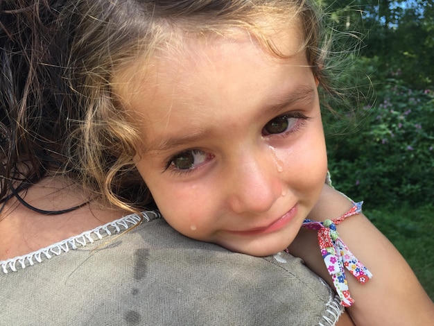 Immagine ritagliata di una madre che porta la figlia che piange contro gli alberi