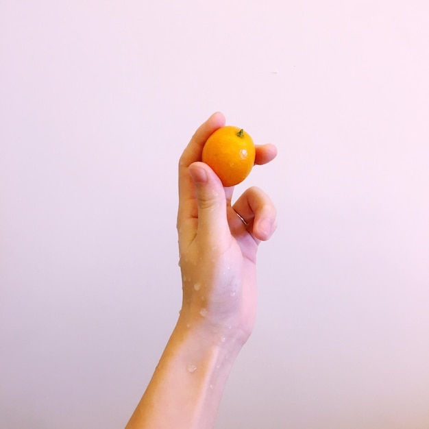 Immagine ritagliata di una mano bagnata che tiene la frutta contro una parete bianca