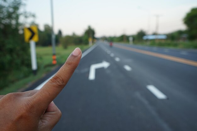 Immagine ritagliata di una persona con la mano sulla strada contro il cielo