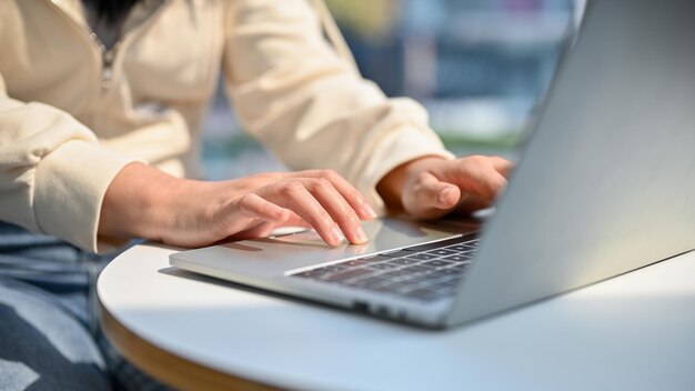 Immagine ritagliata e primo piano di una giovane donna asiatica che utilizza il suo laptop digitando sulla tastiera