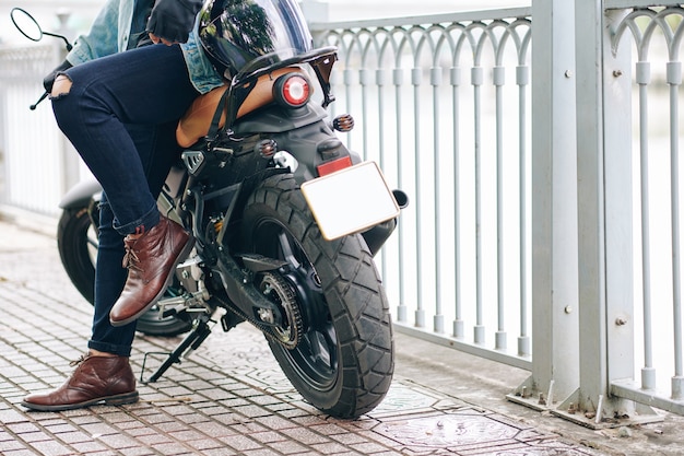 Immagine ritagliata uomo fiducioso in stivali di pelle e jeans strappati appoggiati alla moto