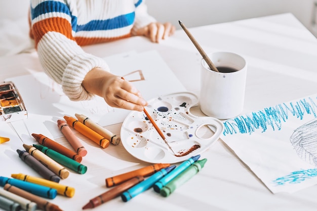 Immagine ritagliata vista dall'alto di una bambina carina che dipinge e disegna con pennello e acquerello sulla scrivania bianca a casa Il bambino in età prescolare carina disegna all'asilo Concetto di infanzia e educazione delle persone