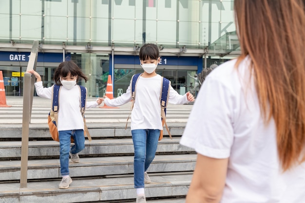 Immagine ritratto di piccoli fratelli asiatici carini che indossano una maschera facciale e prendono una borsa da scuola