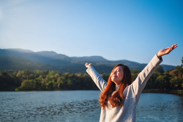 Immagine ritratto di una bella donna asiatica in piedi e aprendo le braccia davanti al lago e alle montagne in una giornata di sole