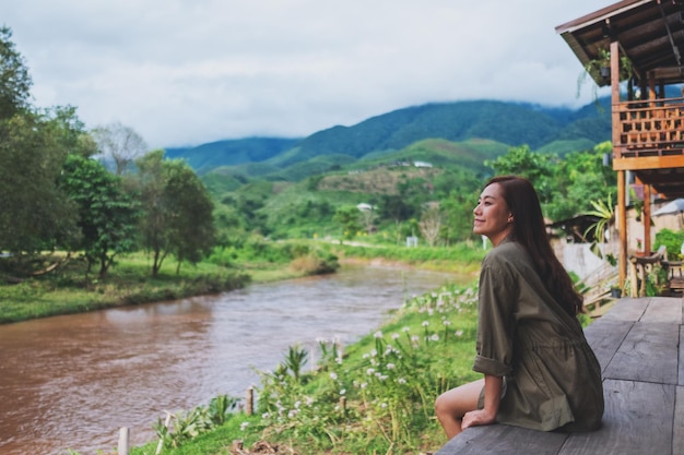 Immagine ritratto di una bella donna asiatica seduta in riva al fiume con montagne e sfondo naturale