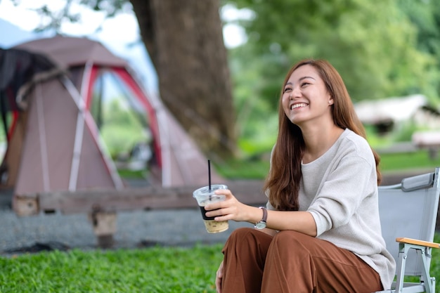 Immagine ritratto di una bella giovane donna asiatica che beve caffè mentre era seduto su una sedia da campeggio con una tenda nel parco