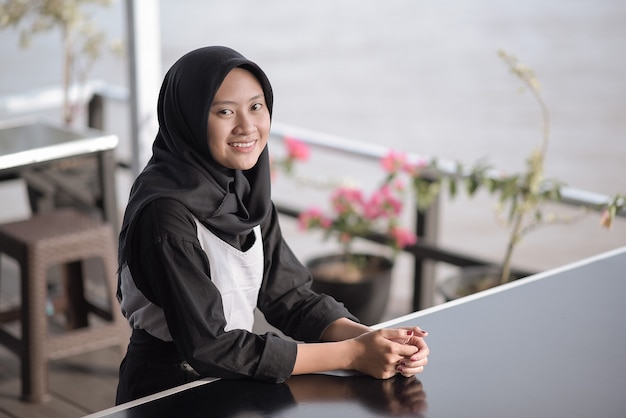 Immagine ritratto di una bellissima giovane donna musulmana seduta al bar e sorridente