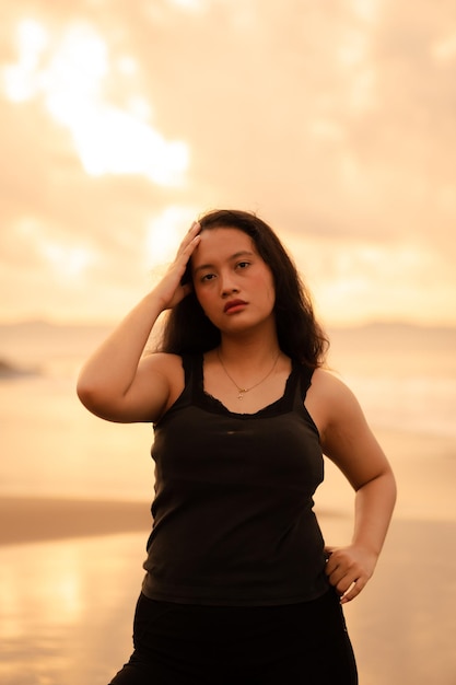 Immagine ritratto di una donna asiatica con i capelli neri e un'espressione arrabbiata in piedi sulla spiaggia nei suoi vestiti neri