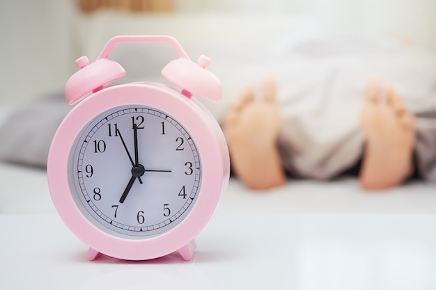 Immagine sfocata delle gambe di una donna addormentata a letto sveglia mattutina che suona messa a fuoco sull'allarme