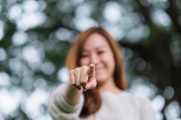 Immagine sfocata di una bella giovane donna asiatica che punta il dito verso la telecamera nel parco