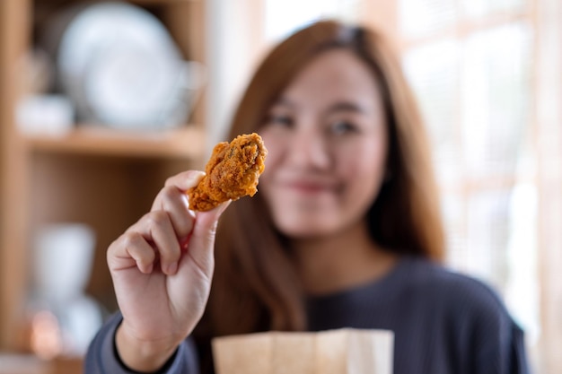 Immagine sfocata di una giovane donna che raccoglie e mostra pollo fritto dal sacchetto di carta per alimenti a casa per il concetto di consegna del cibo