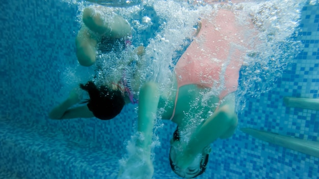 Immagine subacquea di due adolescenti che saltano e si tuffano in piscina in palestra