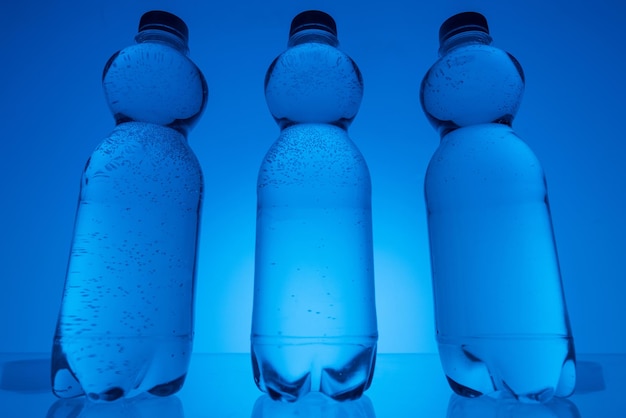Immagine tonica di bottiglie di plastica trasparenti con acqua su sfondo blu neon